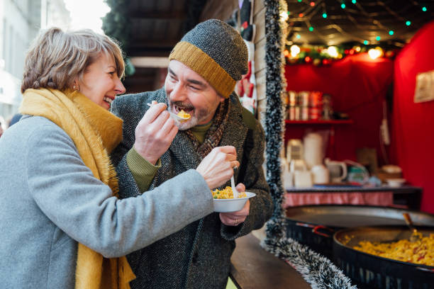 Elderly Couple Eating at Christmas Market Mature couple are enjoying sharing some paella from a christmas market stall food recall stock pictures, royalty-free photos & images