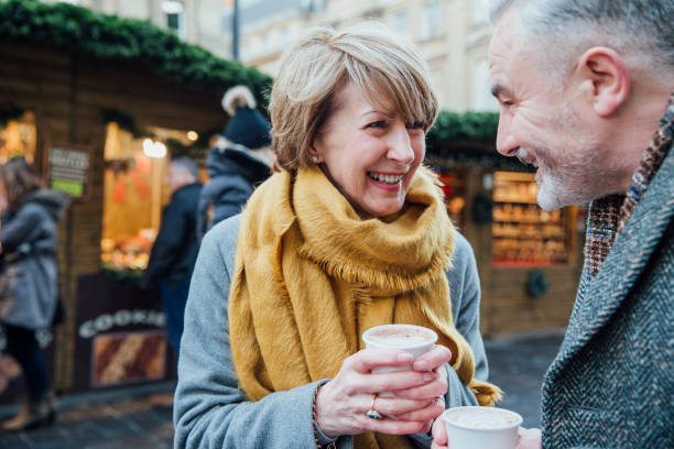 Enjoying Coffee At The Christmas Market Mature couple are enjoying a cup of coffee as they explore the town christmas market. christmas market photos stock pictures, royalty-free photos & images