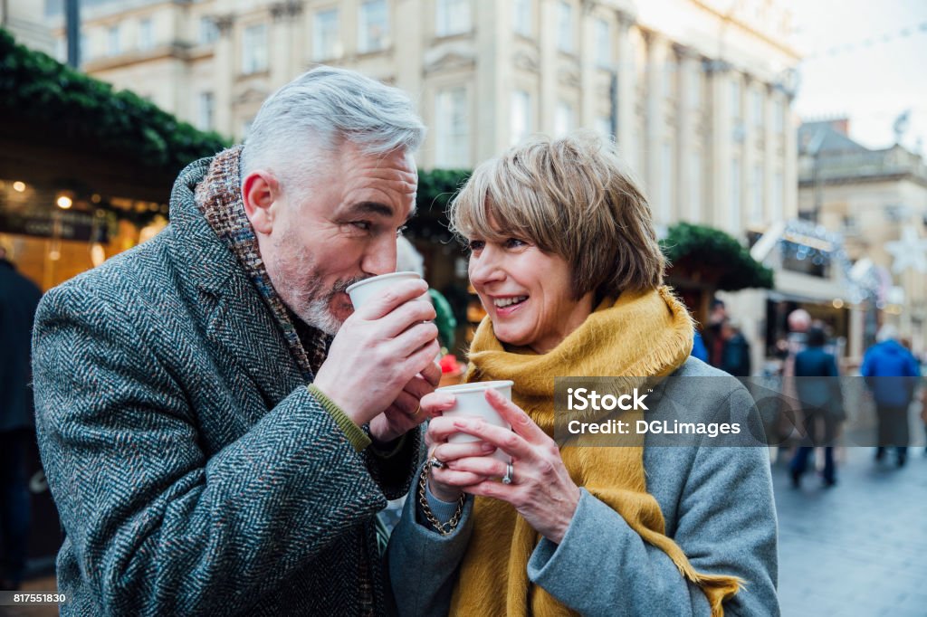Enjoying Coffee At The Christmas Market Mature couple are drinking hot drinks in a town christmas market. Christmas Market Stock Photo