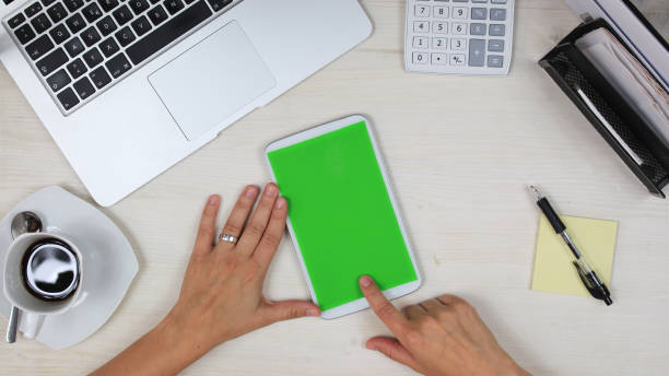istock woman using a mobile phone /  tablet PC with green screen at her desk in the office - top view 817551938