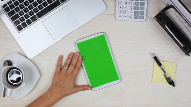 istock woman using a mobile phone /  tablet PC with green screen at her desk in the office - top view 817552320