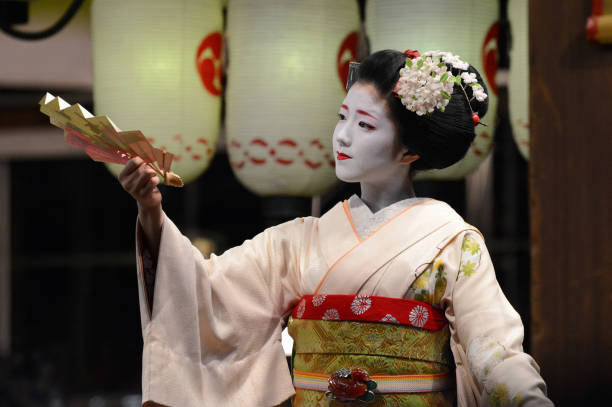 A young geisha entertains onlookers with a dance and fan performance in Kyoto Kyoto, Japan - March 20, 2016 - Young Japanese geisha woman demonstrating slow-moving dance moves at the Yasaka Shrine in Kyoto's Gion District, an area famous for traditional arts and culture preservation. geisha costume stock pictures, royalty-free photos & images