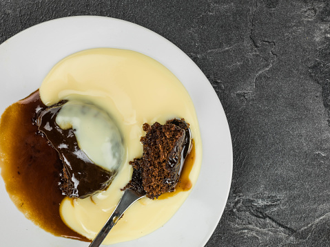 Sticky Toffee Pudding Dessert Served With Hot Custard Against a Black Slate Background