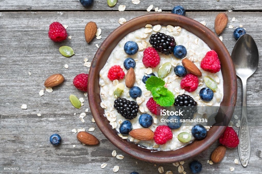 oatmeal porridge with berries and nuts in a bowl with a spoon for healthy breakfast on rustic wooden background oatmeal porridge with berries and nuts in a bowl with a spoon for healthy breakfast on rustic wooden background. top view Berry Stock Photo