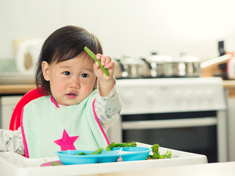 front view of baby girl eating  vegetable at home