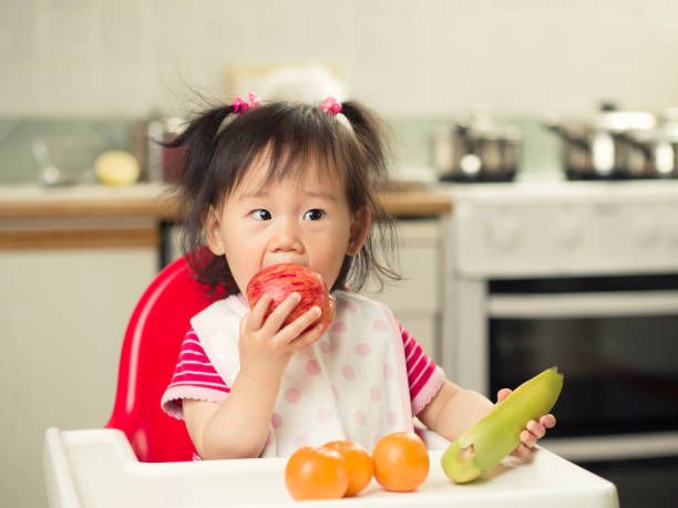 istock baby girl eating fruit at home 817784536