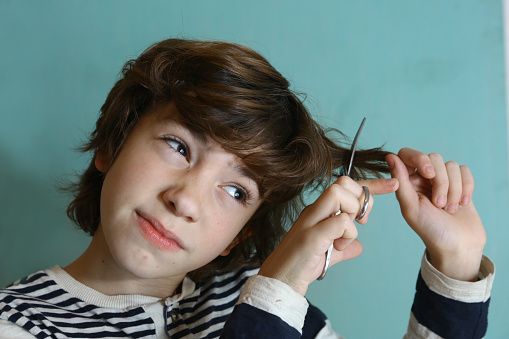 teenager boy cut his hair with scissors close up photo