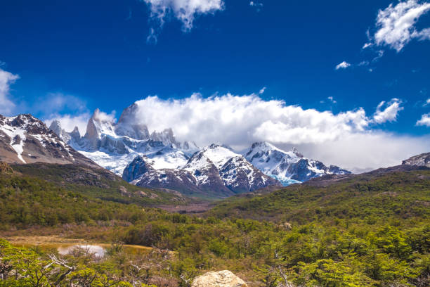istock Landscape with trees, green grass and beautiful snow covered mountains on the back covered with clouds. 817806896