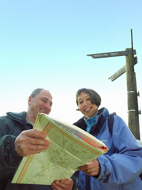 couple takes break from hiking looking at map with direction sign in background - map uk hiking reading fotografías e imágenes de stock