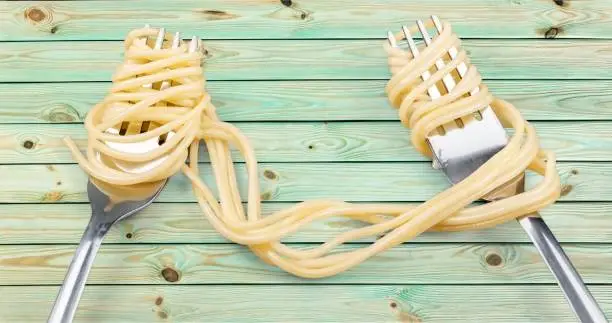 Forks with boiled spaghetti on wooden table background