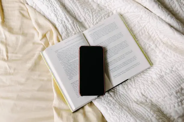 Book open on bed with smart phone on top.