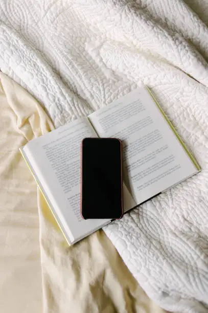 Book open on bed with smart phone on top.