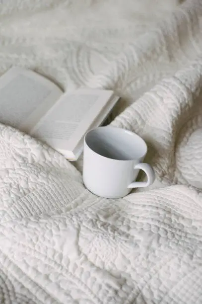 Book open on bed with mug next to it.