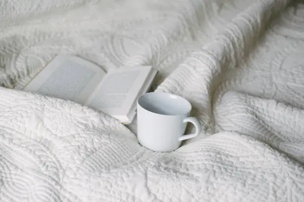 Book open on bed with mug next to it.