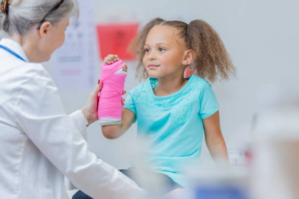 Young patient holds up broken arm Pediatric orthopedic doctor examines an elementary age mixed race girl's broken arm. The girl has a pink cast on her arm. emergency medicine stock pictures, royalty-free photos & images