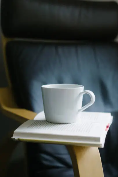 Book open on arm of chair with coffee cup on top.