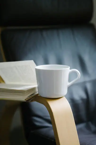 Book open on arm of chair with coffee cup.