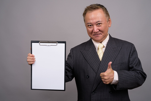 Studio shot of mature Asian businessman holding clipboard against gray background horizontal shot