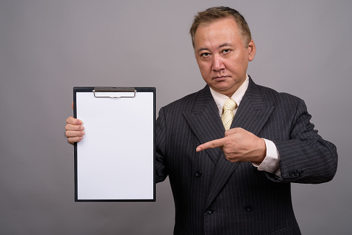 Studio shot of mature Asian businessman holding clipboard against gray background horizontal shot