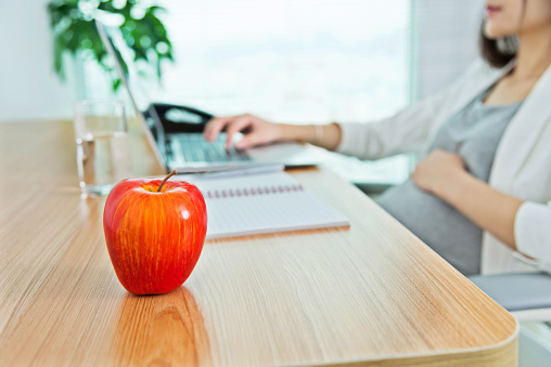 Pregnant woman in office having apple