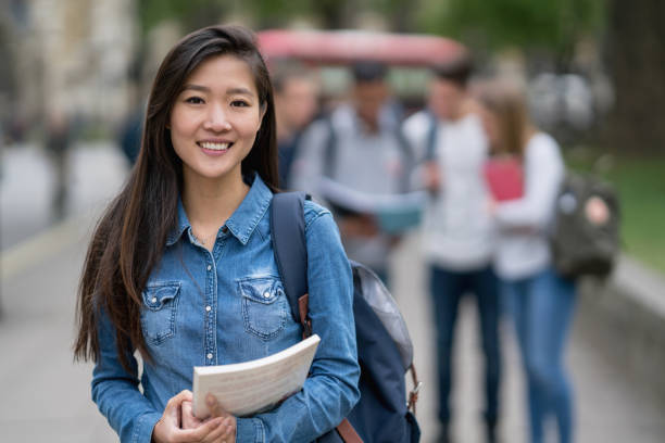 Portrait of an Asian student on the street looking at the camera smiling Portrait of an Asian student on the street looking at the camera smiling with a group at the background - abroad education concepts chinese ethnicity stock pictures, royalty-free photos & images