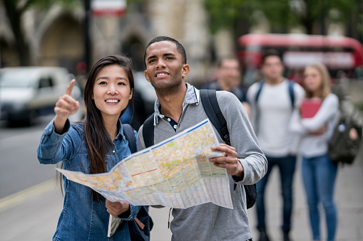 Happy multi-ethnic couple sightseeing in London and holding a map looking for directions. Map was designed from scratch by us.