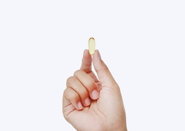 istock Hand holding yellow fish oil capsule isolated on white background. 818101656