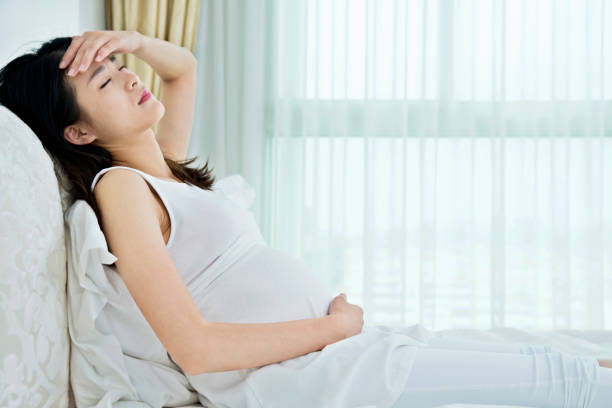 妊娠中の女性がベッドに座って - uncomfortable ストックフォトと画像