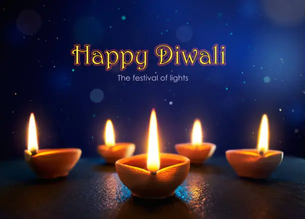 Happy Diwali - Lit diya lamps in the bluish night background