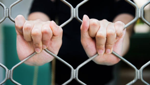 istock Close-up of woman hands on cell bars 818149068