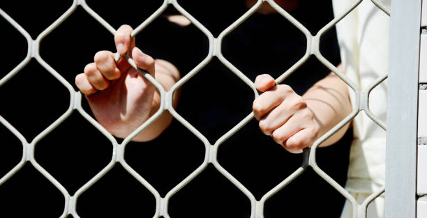 istock Close-up of woman hands on cell bars 818149294