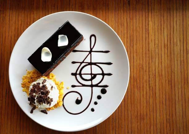 Delicious dark chocolate cake decorated with slice of white chocolate curls, whipping cream and chocolate music note in white plate on wooden table. stock photo
