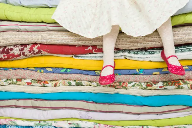 Photo of Legs of a little girl sitting on a pile of colorful mattresses. Decorations for the fairy tale The princess on a Pea