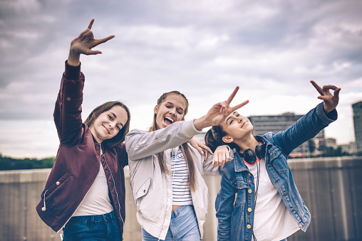 three happy teenage girls dancing and raising arms outdoors