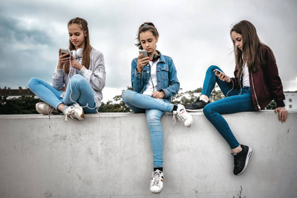 three teenage girls with smartphones on concrete wall stock photo