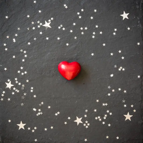 Photo of Small red heart on the black background with silver stars. Hearts and stars on a black board. Background. Valentine's and Christmas.