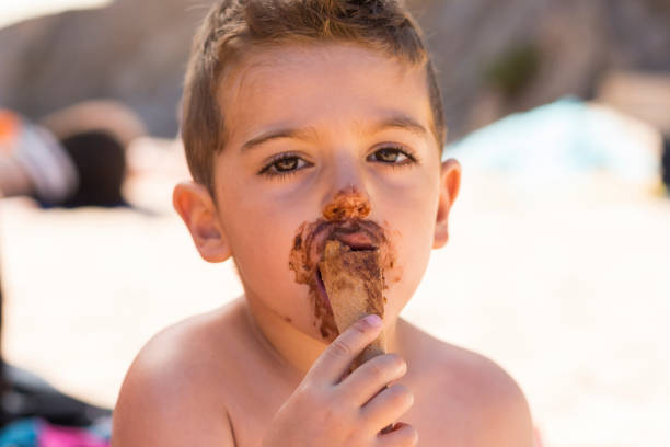 Close-up shot of a young boy eating a chocolate ice cream on a stick, with a joyful expression on his face.