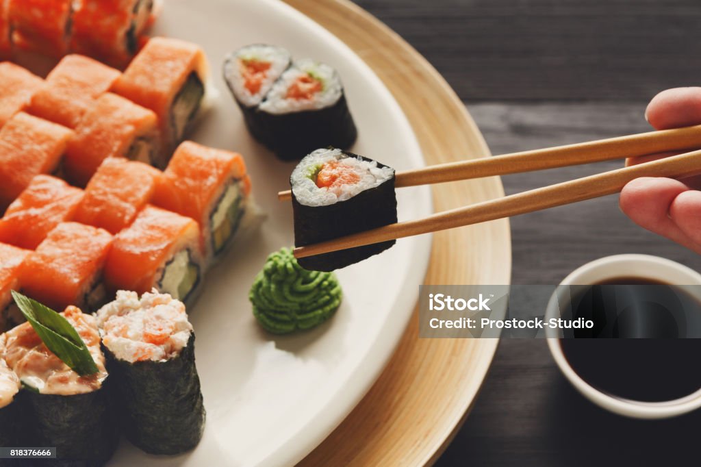 Eating sushi and rolls in japanese restaurant Eating roll sushi in japanese restaurant, hand with chopsticks closeup. Female has dinner Above Stock Photo