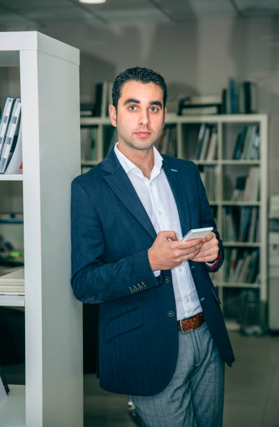 istock Businessman holding smartphone leaning on a bookcase 818386896