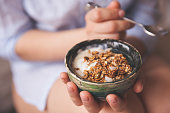 Young woman with muesli bowl. Girl eating breakfast cereals with nuts, pumpkin seeds, oats and yogurt in bowl. Girl holding homemade granola. Healthy snack or breakfst in the morning.