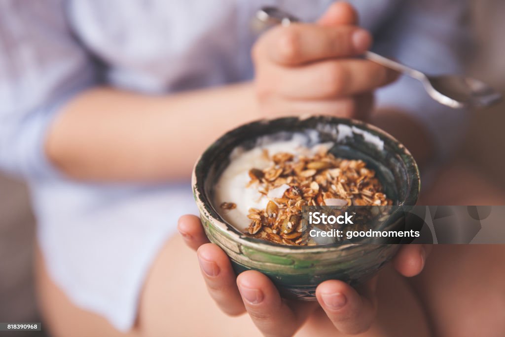 Young woman with muesli bowl. Girl eating breakfast cereals with nuts, pumpkin seeds, oats and yogurt in bowl. Girl holding homemade granola. Healthy snack or breakfst in the morning. Granola Stock Photo