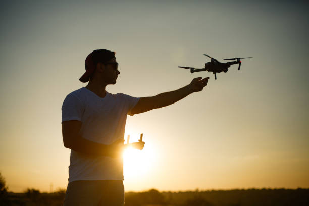 istock Silhouette of a man catching drone with one hand and remote controller in another hand on sunset. Safe quadcopter landing on the pilot's palm 818399552