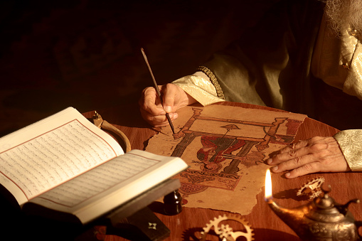 Detail shot of an old and historic Islamic scientist is working in his studio writing, reading and exploring.