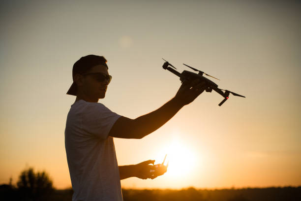 istock Silhouette of a man holding small compact drone and remote controller in his hands. Pilot launches quadcopter from his palm on sunset. Drone ready to take off 818400934