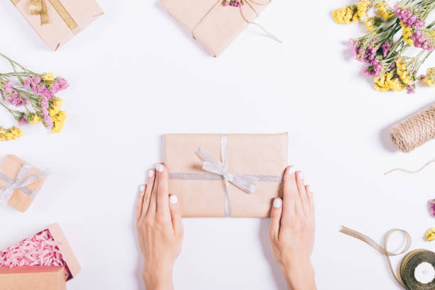 istock Female hands holding a gift with a ribbon on a white table with decorations 818410790