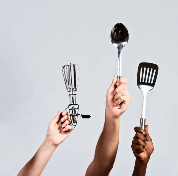 istock Hands hold kitchen utensils aloft against gray 818435368