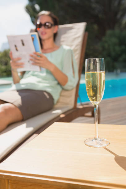 istock Woman reading book by pool with champagne in foreground 818455446