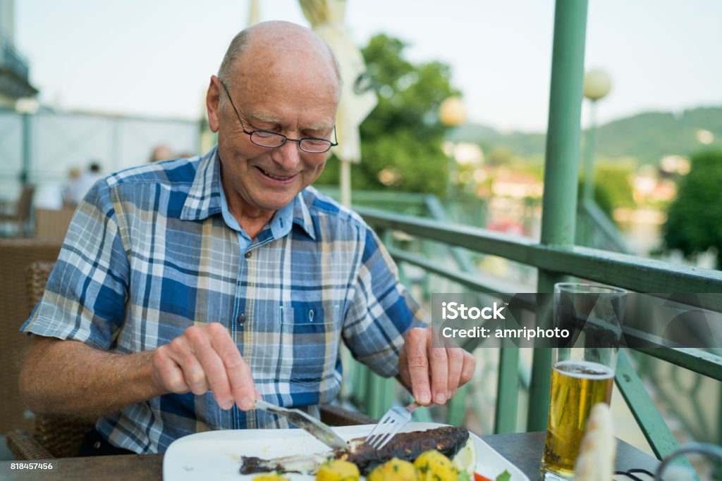 Car Trip, senior man enjoying lunch happy senior man eating grilled fish outside on restaurant terrace Eating Stock Photo