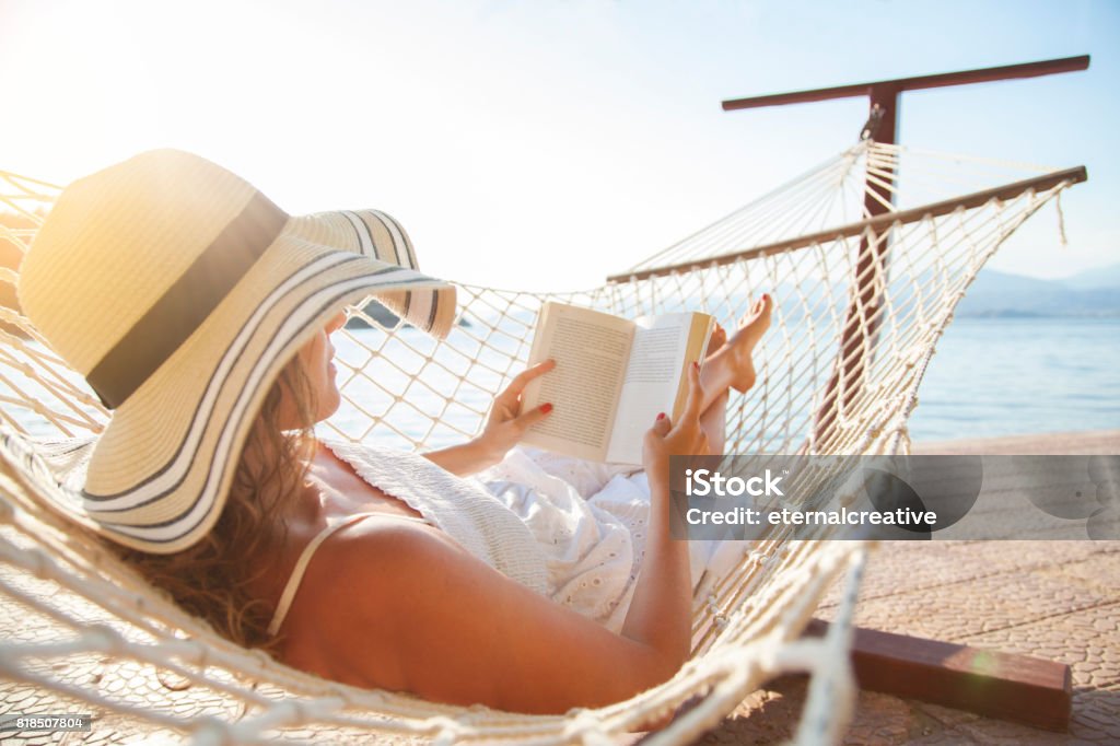 Mujer joven, leyendo un libro en una hamaca al atardecer. - Foto de stock de Leer libre de derechos