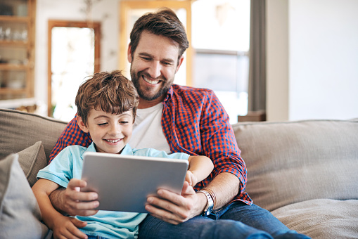 Shot of a father and son sitting on the sofa and using a digital tablet together